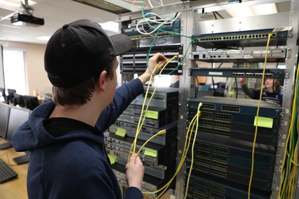 A male student plugging RJ-45 cables into a server rack.